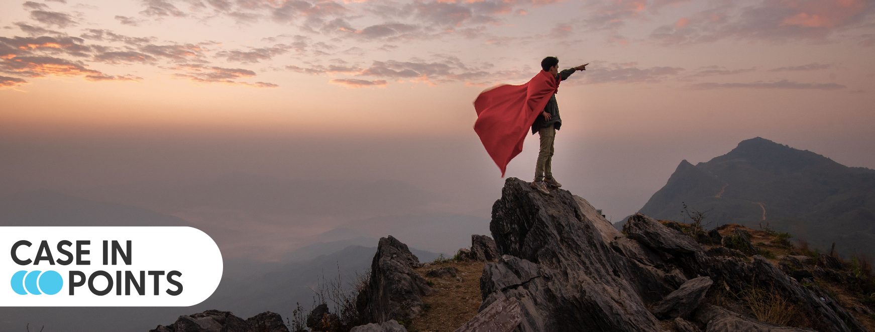 Person on mountain top with cape pointing to the horizon.